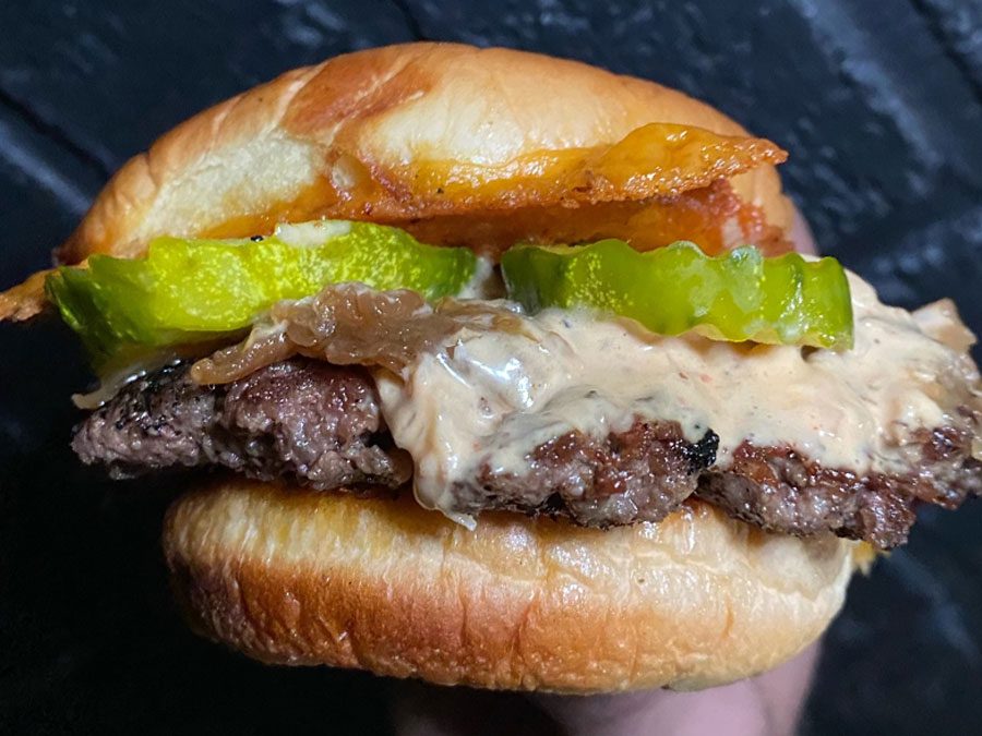 A close-up of a cheeseburger featuring a beef patty, creamy sauce, Grillo's Pickles, onions, and a soft bun.